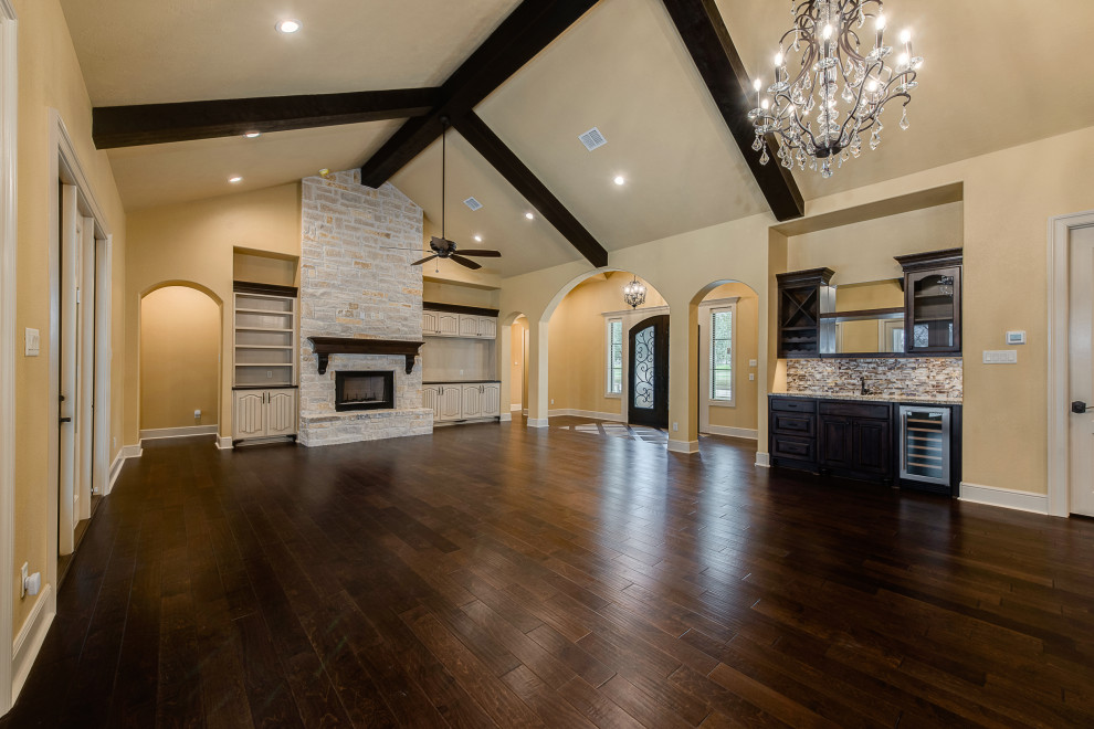 Large mediterranean open plan games room in Other with a home bar, yellow walls, dark hardwood flooring, a standard fireplace, a stone fireplace surround, a wall mounted tv and brown floors.
