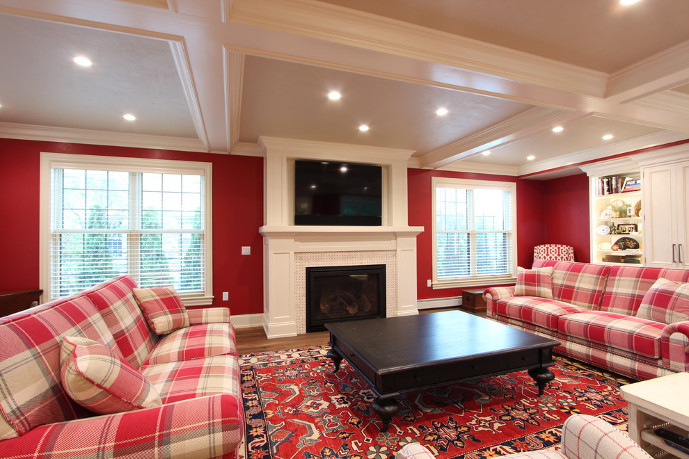 他の地域にあるお手頃価格の広いトランジショナルスタイルのおしゃれな独立型ファミリールーム (赤い壁、無垢フローリング、標準型暖炉、タイルの暖炉まわり、壁掛け型テレビ、茶色い床) の写真
