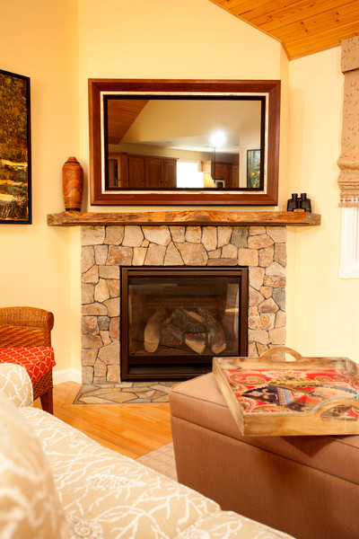 Imagen de sala de estar tradicional con paredes amarillas, suelo de madera clara, chimenea de esquina y marco de chimenea de piedra