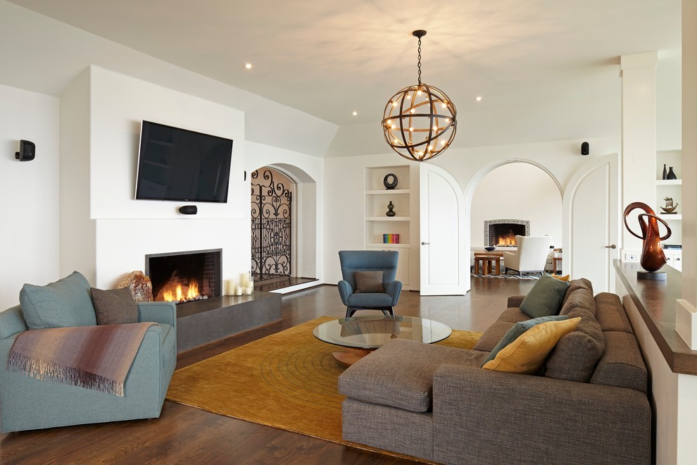 Imagen de sala de estar abierta mediterránea con paredes blancas, suelo de madera oscura, todas las chimeneas, televisor colgado en la pared y alfombra