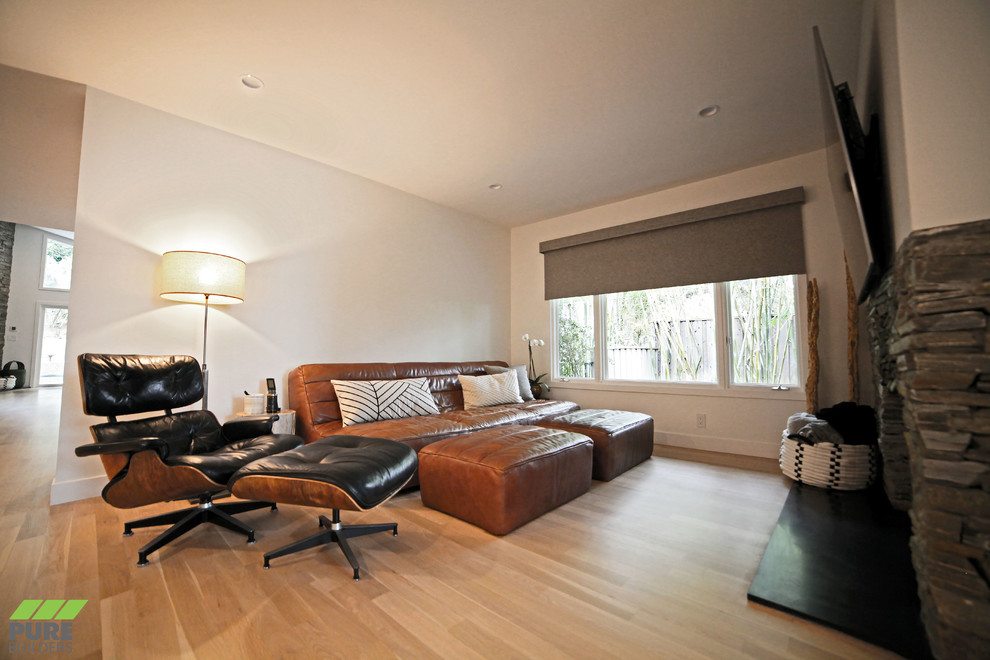 Пример оригинального дизайна: большая открытая гостиная комната в современном стиле с белыми стенами, светлым паркетным полом, стандартным камином, фасадом камина из камня, телевизором на стене и бежевым полом