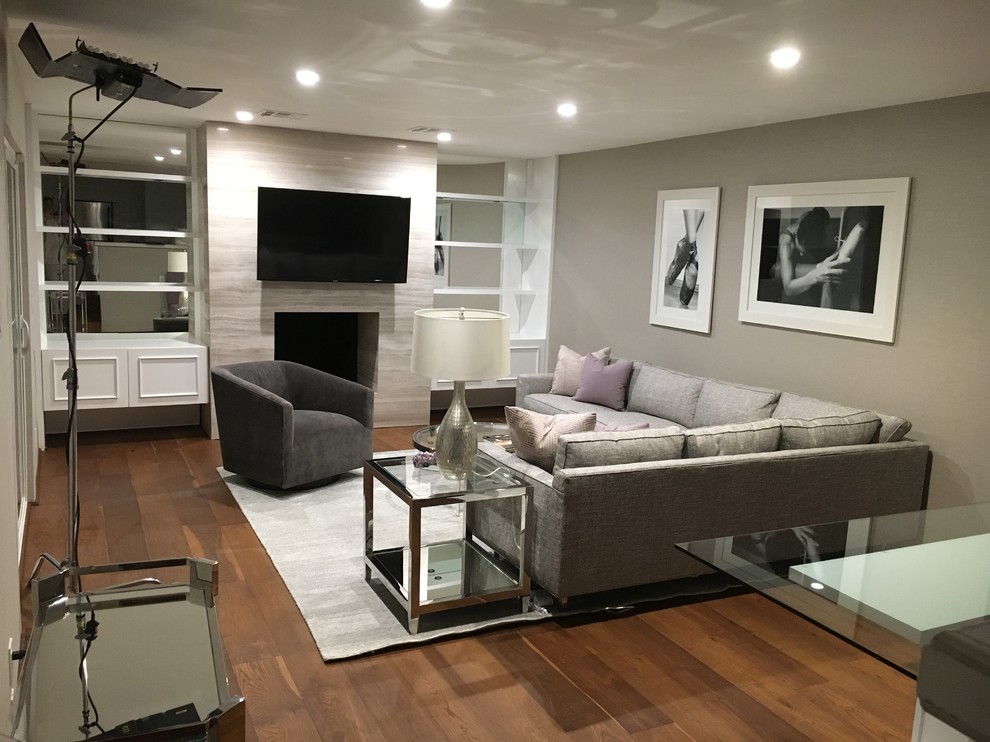 Abgetrenntes, Mittelgroßes Modernes Wohnzimmer mit grauer Wandfarbe, braunem Holzboden, Kamin, Kaminumrandung aus Stein, TV-Wand und braunem Boden in Los Angeles