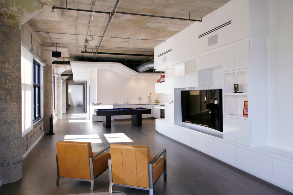 Diseño de sala de estar abierta industrial con suelo de madera oscura, pared multimedia y paredes blancas