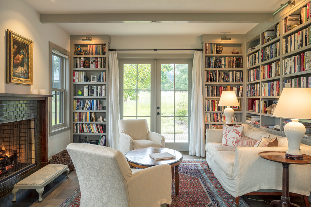 На фото: гостиная комната в стиле кантри с с книжными шкафами и полками, белыми стенами, стандартным камином, фасадом камина из плитки и ковром на полу