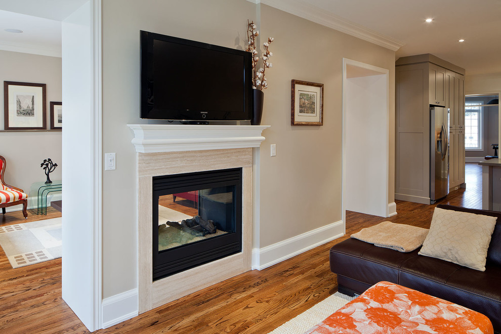 Ejemplo de sala de estar abierta clásica renovada pequeña con paredes grises, suelo de madera en tonos medios, chimenea de doble cara, marco de chimenea de piedra y televisor colgado en la pared