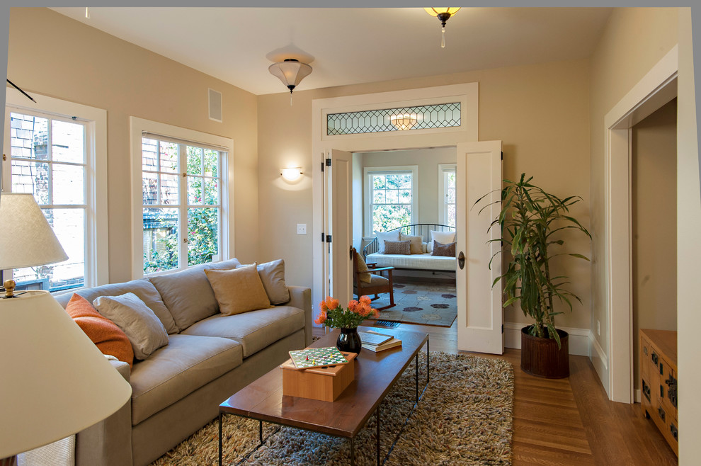 Imagen de sala de estar con biblioteca cerrada de estilo americano de tamaño medio con paredes beige, suelo de madera clara y televisor retractable