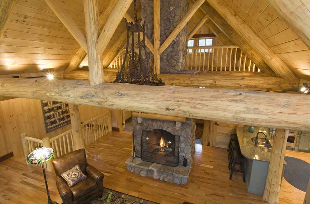 Modelo de sala de estar abierta rural de tamaño medio sin televisor con paredes beige, suelo de madera clara, todas las chimeneas y marco de chimenea de piedra