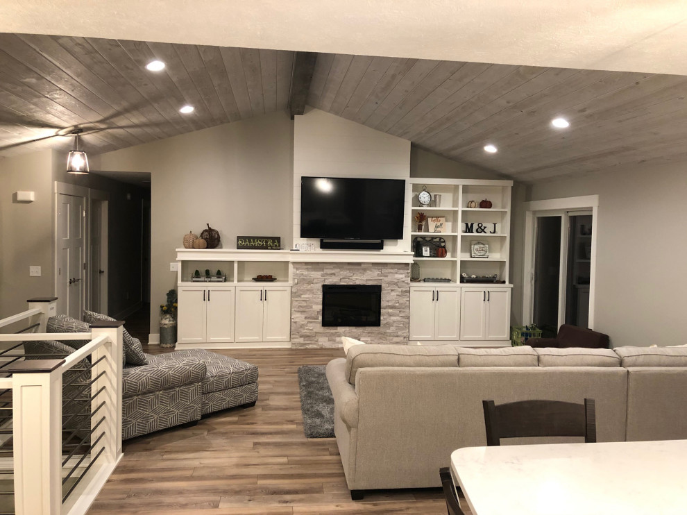 This is an example of a medium sized traditional open plan games room in Grand Rapids with grey walls, vinyl flooring, a stone fireplace surround, a wall mounted tv, brown floors and a standard fireplace.