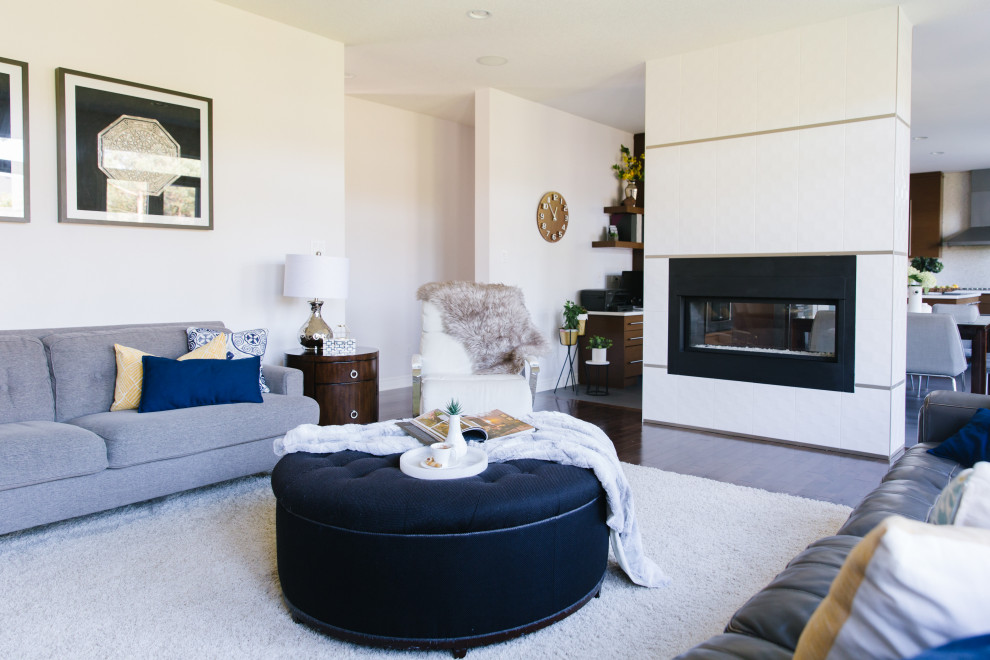 На фото: гостиная комната в современном стиле с серыми стенами, паркетным полом среднего тона, двусторонним камином, фасадом камина из плитки, телевизором на стене и коричневым полом