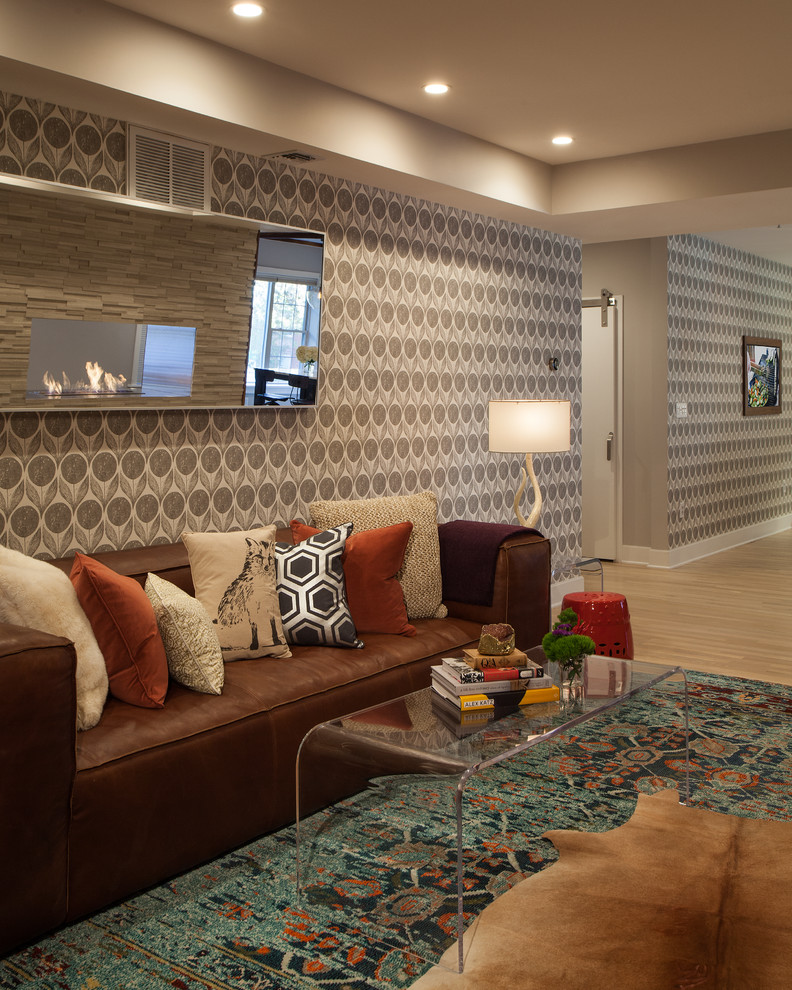 Diseño de sala de estar abierta ecléctica pequeña con paredes grises, suelo de madera clara, chimenea de doble cara, marco de chimenea de piedra, pared multimedia y suelo beige