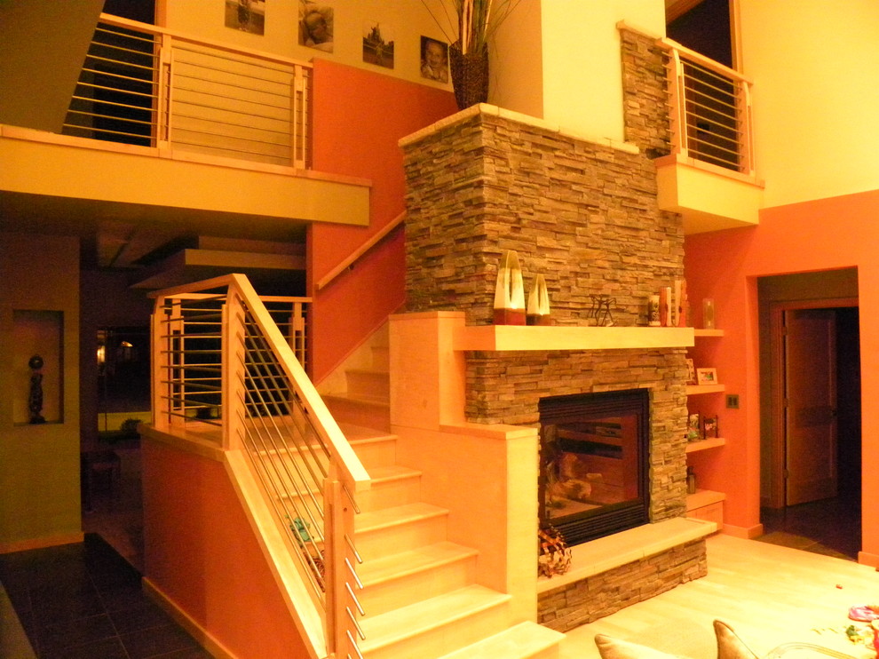 This is an example of a large contemporary open plan games room in Milwaukee with orange walls, light hardwood flooring, a standard fireplace, a brick fireplace surround and no tv.
