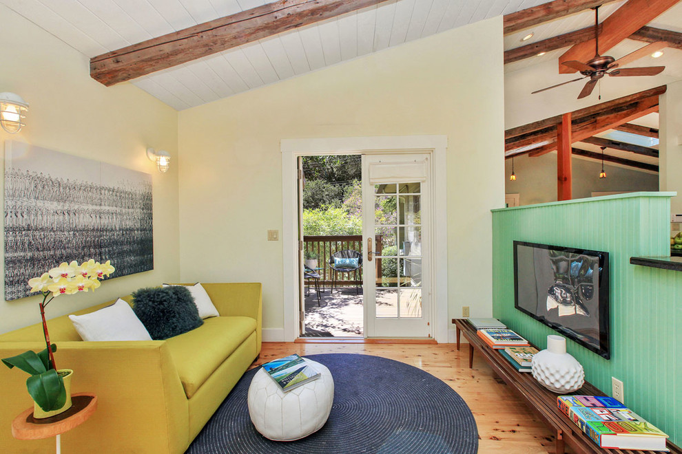 Modelo de sala de estar abierta de estilo de casa de campo pequeña sin chimenea con paredes amarillas, suelo de madera en tonos medios y televisor colgado en la pared