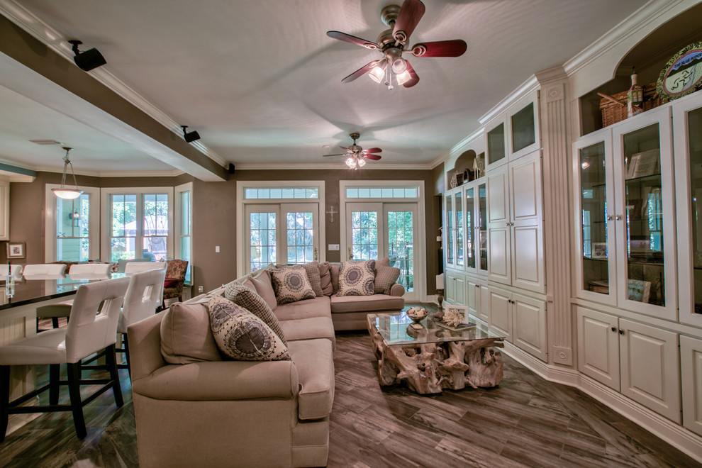Foto de sala de estar abierta clásica de tamaño medio con paredes beige, suelo de madera oscura, televisor retractable y suelo marrón