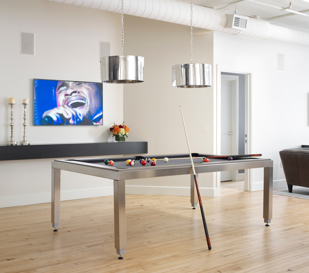 This is an example of an industrial open plan games room in Chicago with white walls, light hardwood flooring and a wall mounted tv.