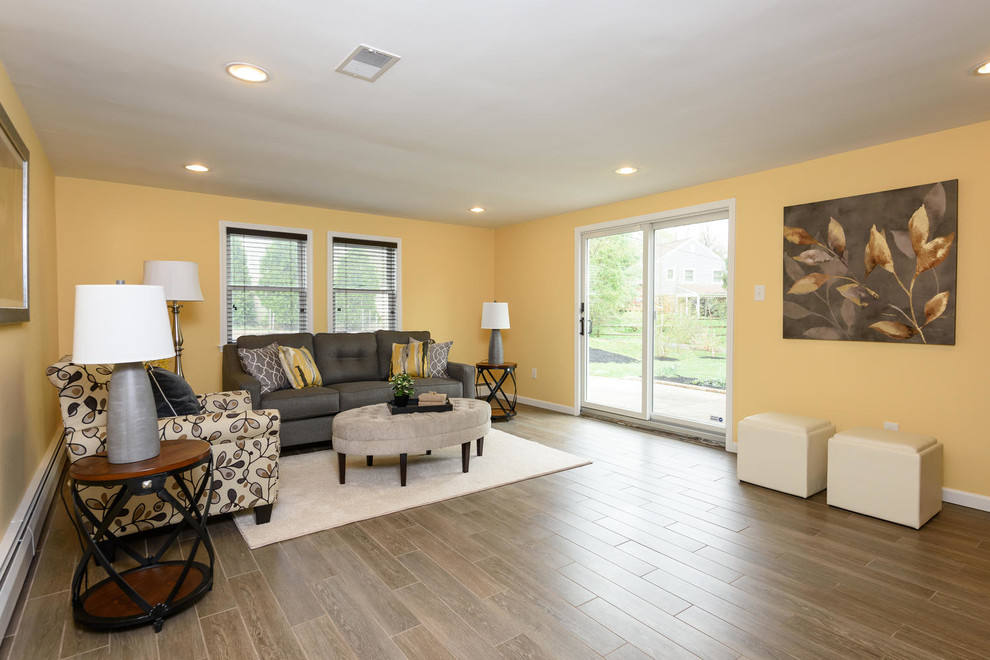 Cette image montre une grande salle de séjour traditionnelle fermée avec un mur jaune, un sol en bois brun et un sol gris.