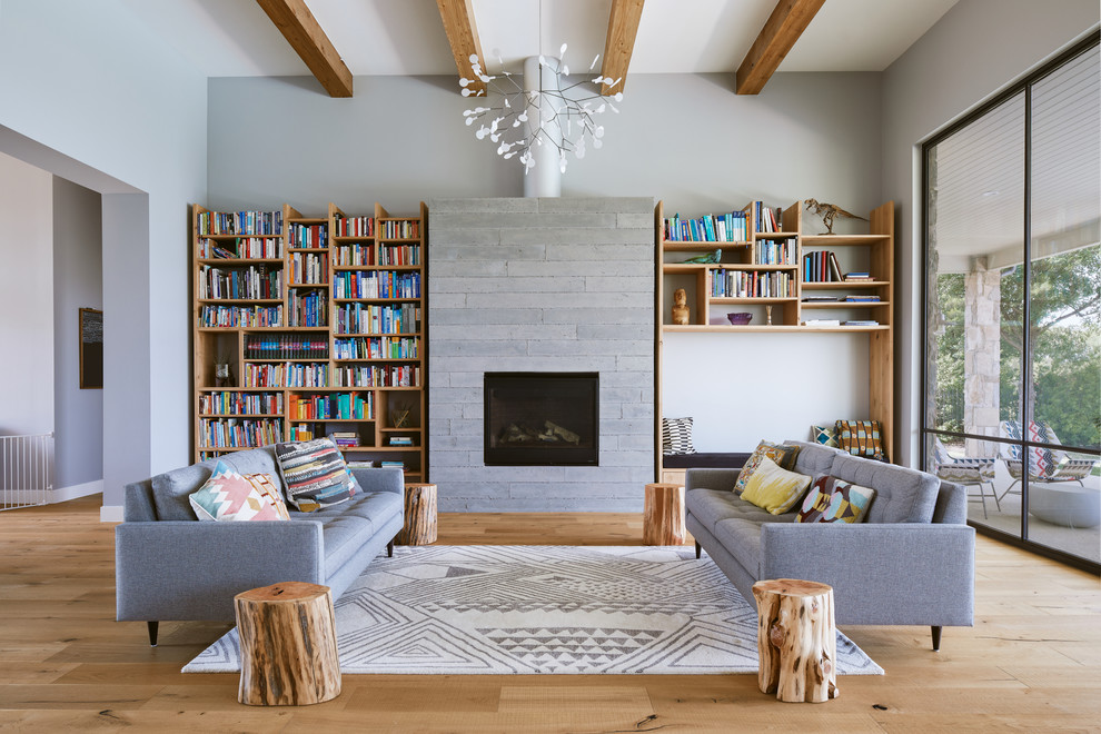 Esempio di un soggiorno design con libreria, pareti grigie, parquet chiaro, camino classico e cornice del camino in cemento