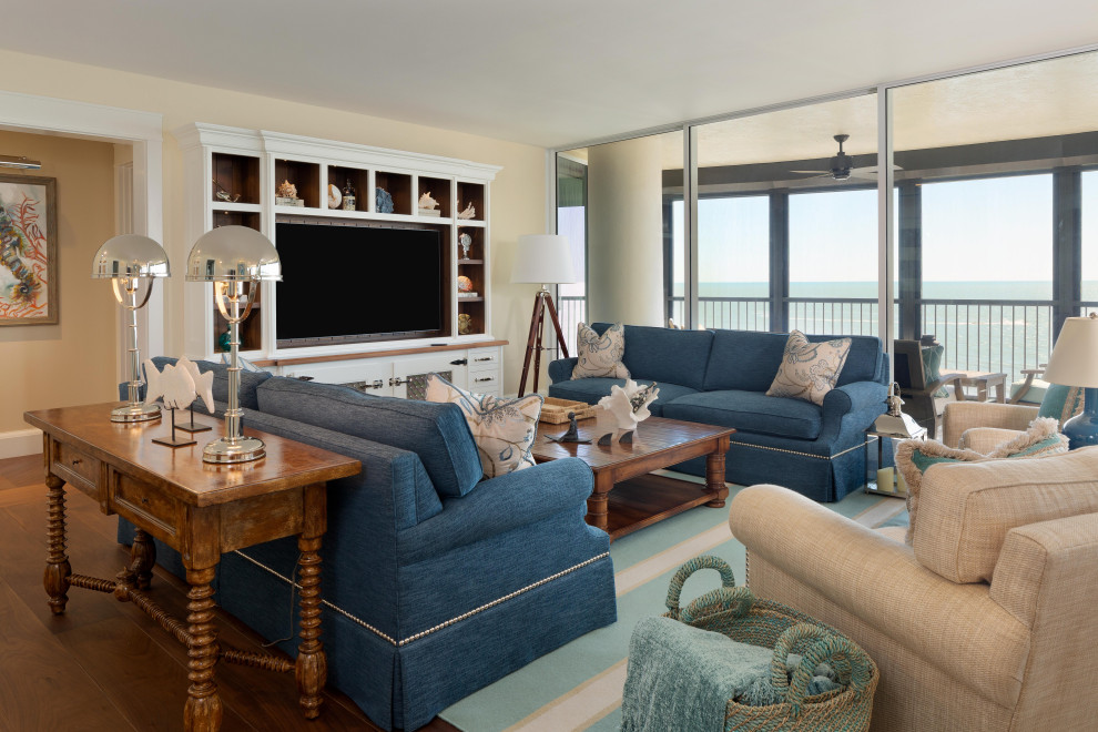 На фото: большая гостиная комната в морском стиле с бежевыми стенами, паркетным полом среднего тона, мультимедийным центром и синим диваном без камина
