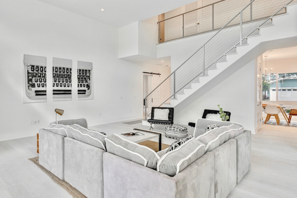 Cette image montre une grande salle de séjour minimaliste ouverte avec un mur blanc, parquet clair et un sol blanc.