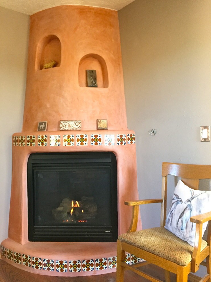 アルバカーキにあるお手頃価格の中くらいなサンタフェスタイルのおしゃれな独立型ファミリールーム (ライブラリー、グレーの壁、無垢フローリング、コーナー設置型暖炉、漆喰の暖炉まわり) の写真
