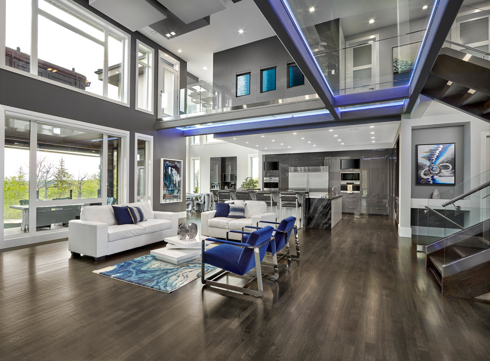 This is an example of an expansive contemporary open plan games room in Edmonton with grey walls, dark hardwood flooring, a two-sided fireplace, a plastered fireplace surround, a wall mounted tv and brown floors.
