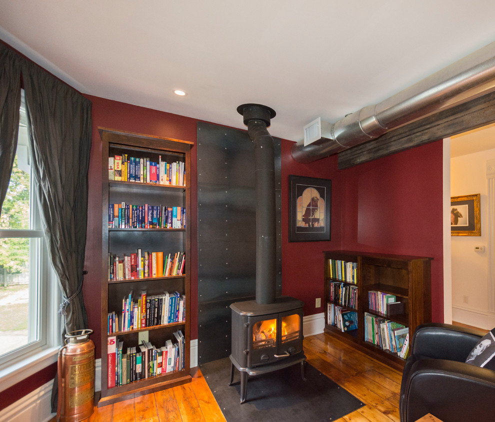 Immagine di un piccolo soggiorno boho chic aperto con libreria, pareti rosse, pavimento in legno massello medio, camino classico e cornice del camino in metallo