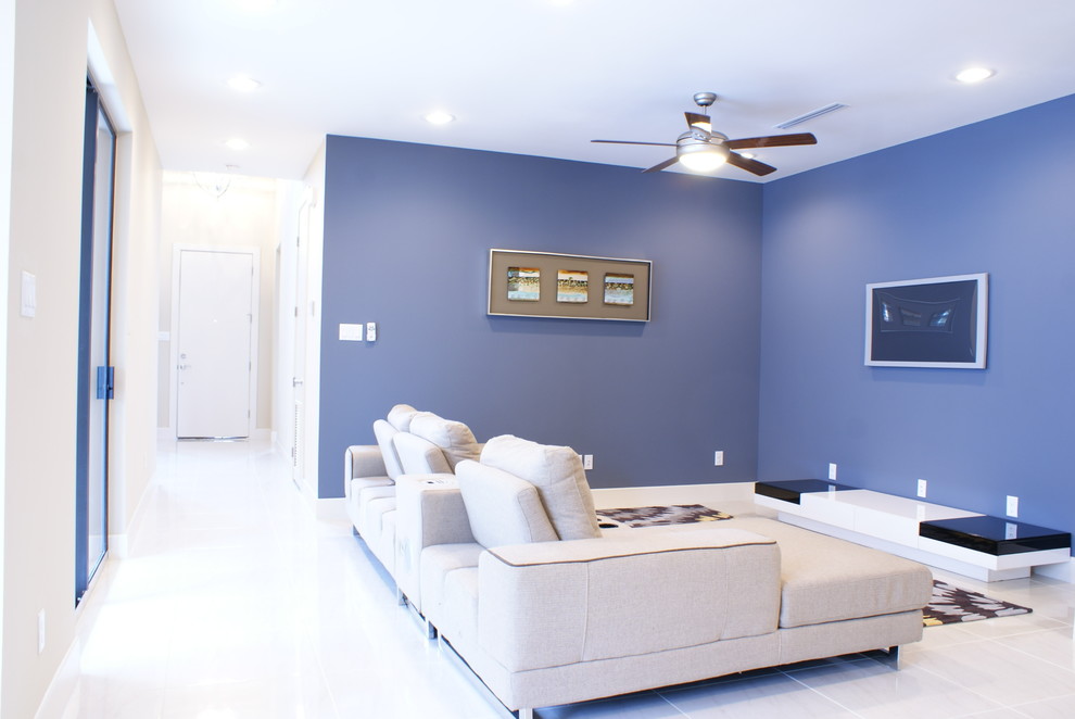 Diseño de sala de estar abierta actual grande con paredes azules, suelo de baldosas de porcelana y televisor colgado en la pared