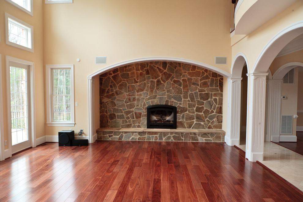 Modelo de sala de estar abierta clásica renovada extra grande con suelo de madera en tonos medios y marco de chimenea de piedra