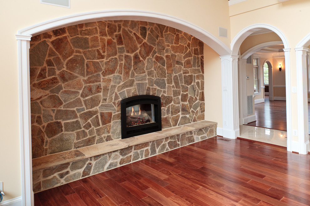 Foto de sala de estar abierta tradicional renovada extra grande con suelo de madera en tonos medios y marco de chimenea de piedra