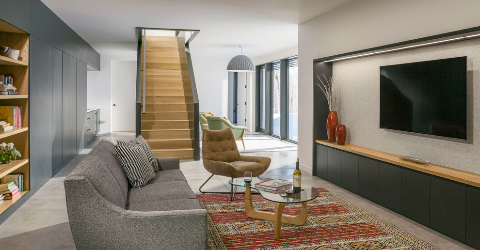 Immagine di un soggiorno design con pareti bianche, pavimento in cemento, TV a parete e pavimento grigio