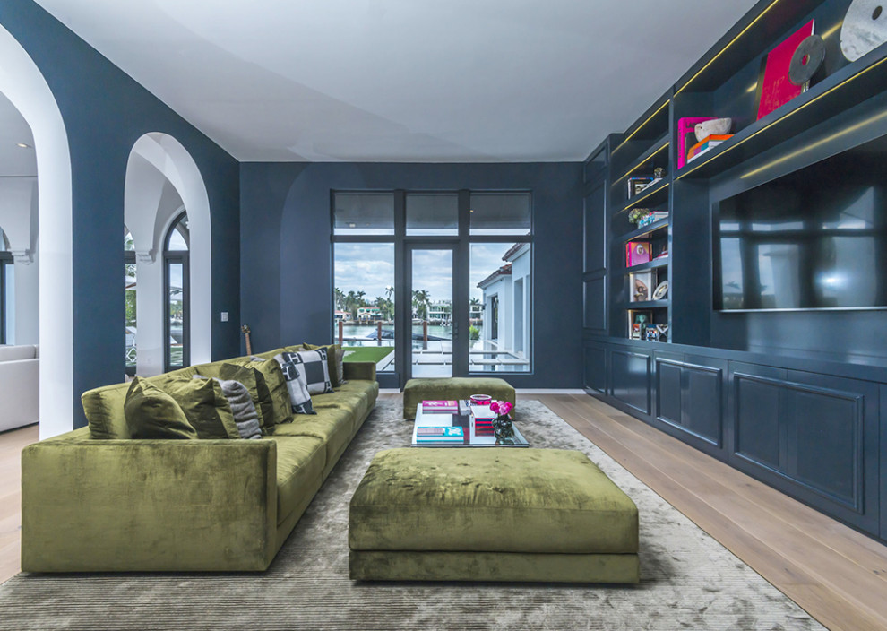 Пример оригинального дизайна: огромная открытая гостиная комната в стиле модернизм с с книжными шкафами и полками, синими стенами, паркетным полом среднего тона, мультимедийным центром, коричневым полом и панелями на части стены