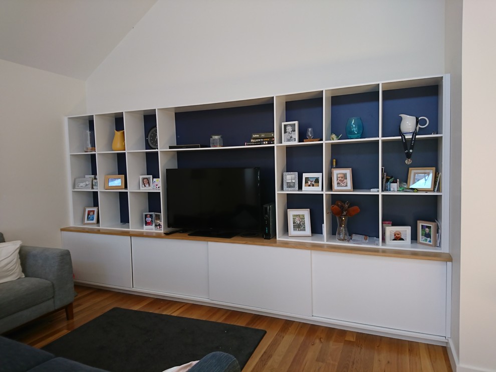Ejemplo de sala de estar abierta moderna grande con paredes blancas, suelo de madera en tonos medios y pared multimedia