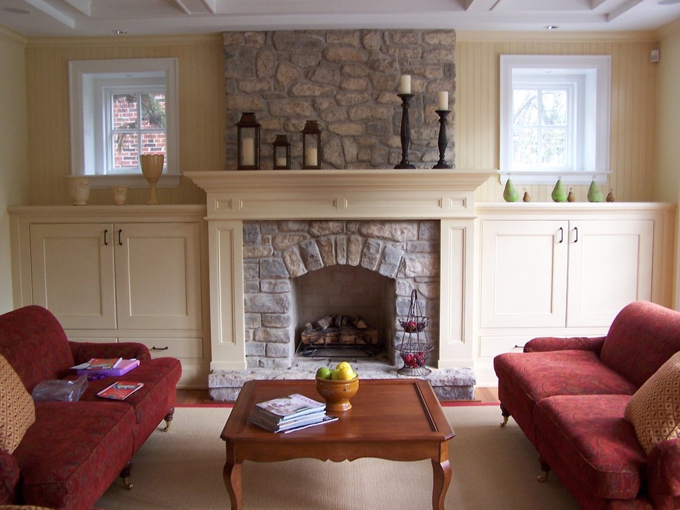 Imagen de sala de estar abierta clásica pequeña con paredes amarillas, suelo de madera en tonos medios, todas las chimeneas y marco de chimenea de piedra