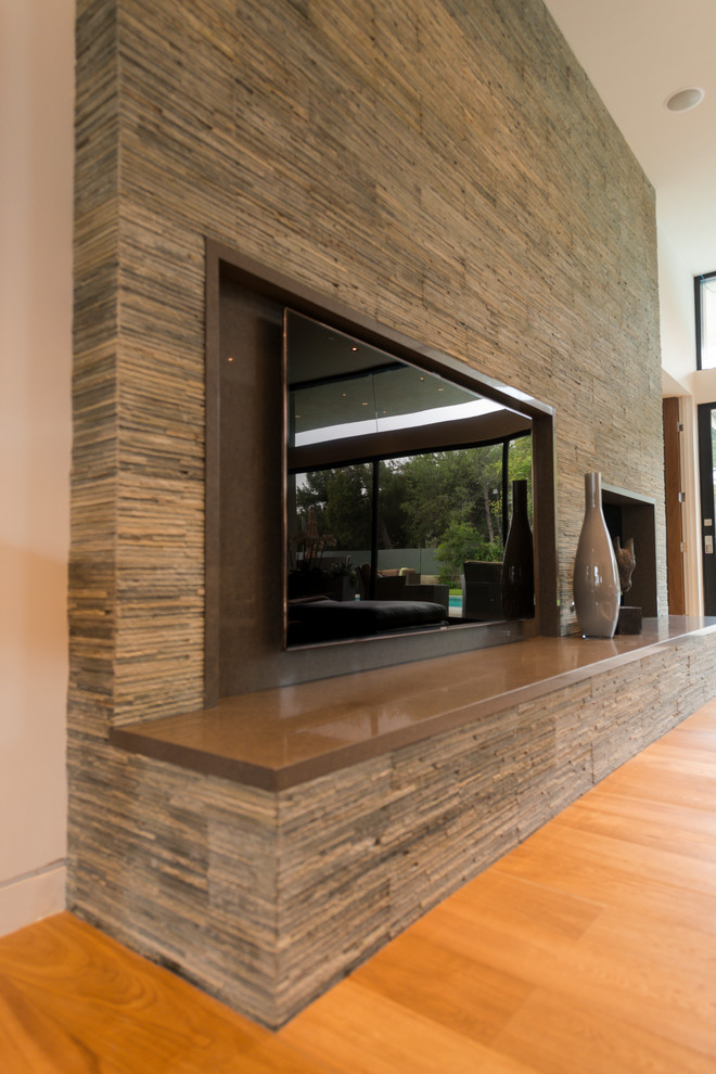 Photo of an expansive modern formal open plan living room feature wall in Los Angeles with grey walls, light hardwood flooring, a standard fireplace, a stacked stone fireplace surround, a built-in media unit, beige floors and a drop ceiling.