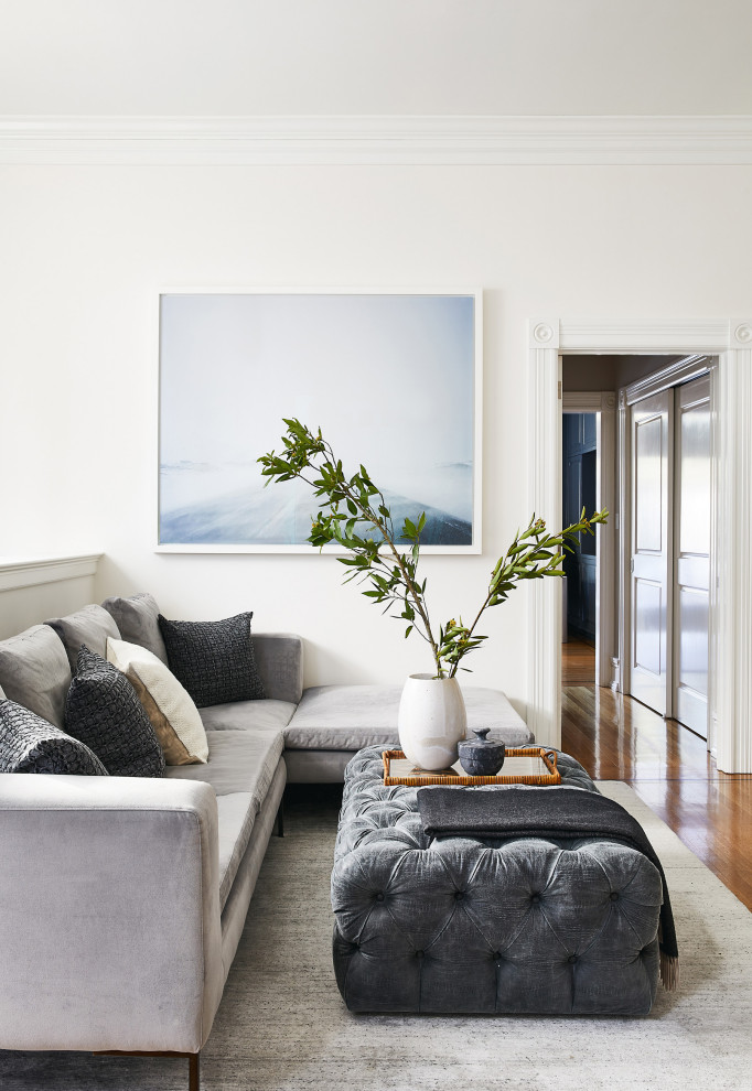 Modelo de sala de estar clásica renovada con paredes blancas, suelo de madera en tonos medios y suelo marrón