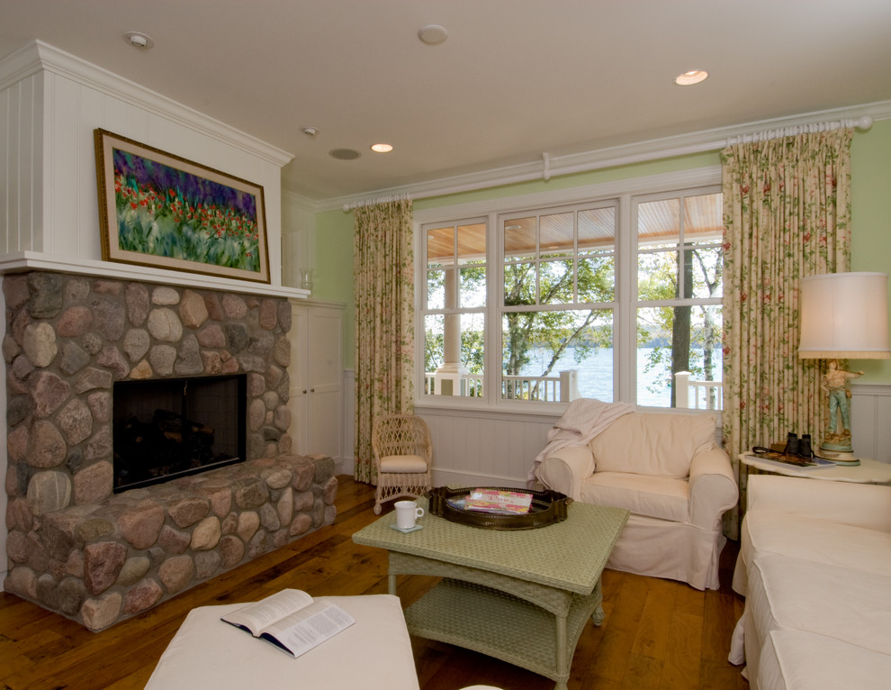 Aménagement d'une salle de séjour bord de mer de taille moyenne et fermée avec un mur vert, une cheminée standard, un manteau de cheminée en pierre, un sol en bois brun, un sol marron et boiseries.