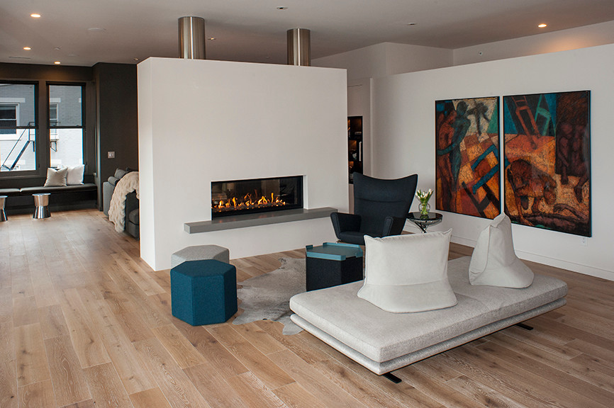 Diseño de sala de estar tipo loft actual de tamaño medio sin televisor con paredes blancas, suelo de madera en tonos medios, chimenea de doble cara, marco de chimenea de yeso y suelo marrón