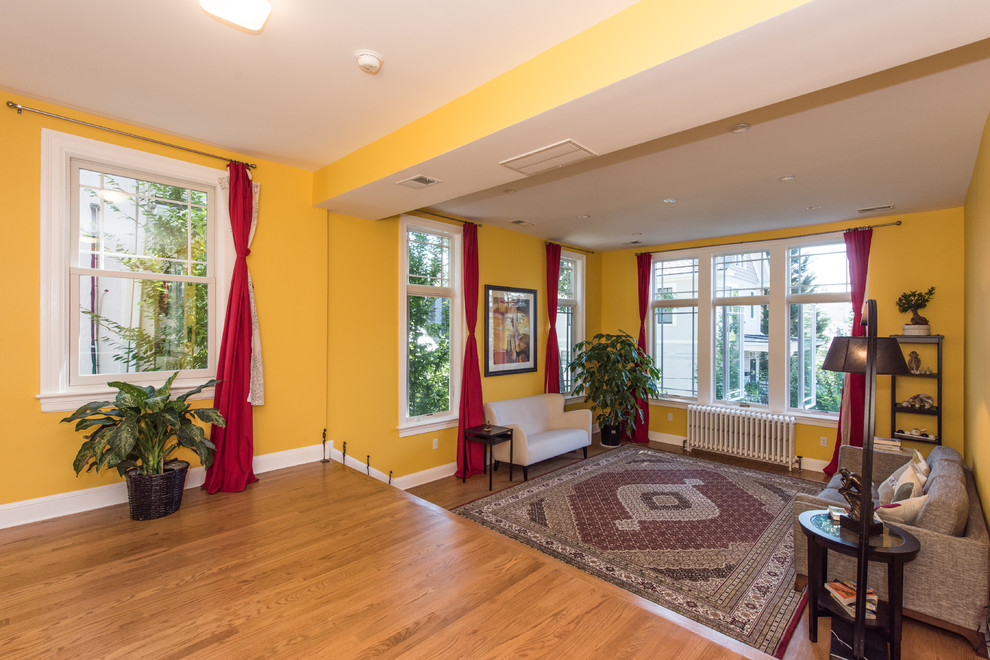 Diseño de sala de estar con biblioteca abierta bohemia de tamaño medio con paredes amarillas, suelo de madera en tonos medios y suelo beige