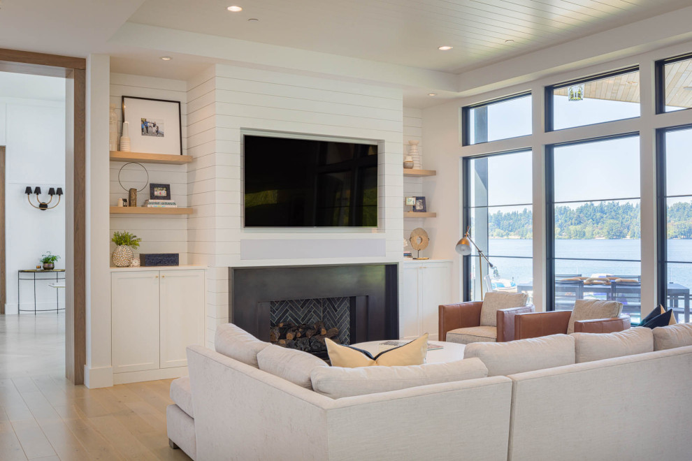 シアトルにあるビーチスタイルのおしゃれなLDK (白い壁、淡色無垢フローリング、標準型暖炉、金属の暖炉まわり、埋込式メディアウォール、三角天井、塗装板張りの壁) の写真