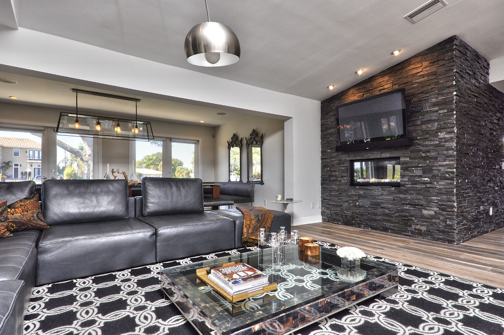 Großes, Offenes Modernes Wohnzimmer mit grauer Wandfarbe, braunem Holzboden, Gaskamin, Kaminumrandung aus Stein und TV-Wand in Tampa