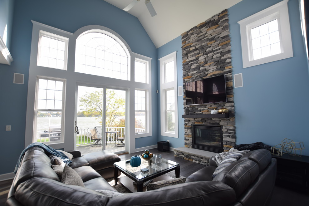 Réalisation d'une grande salle de séjour minimaliste ouverte avec un mur bleu, parquet foncé, une cheminée standard, un manteau de cheminée en pierre, un téléviseur dissimulé et un sol gris.