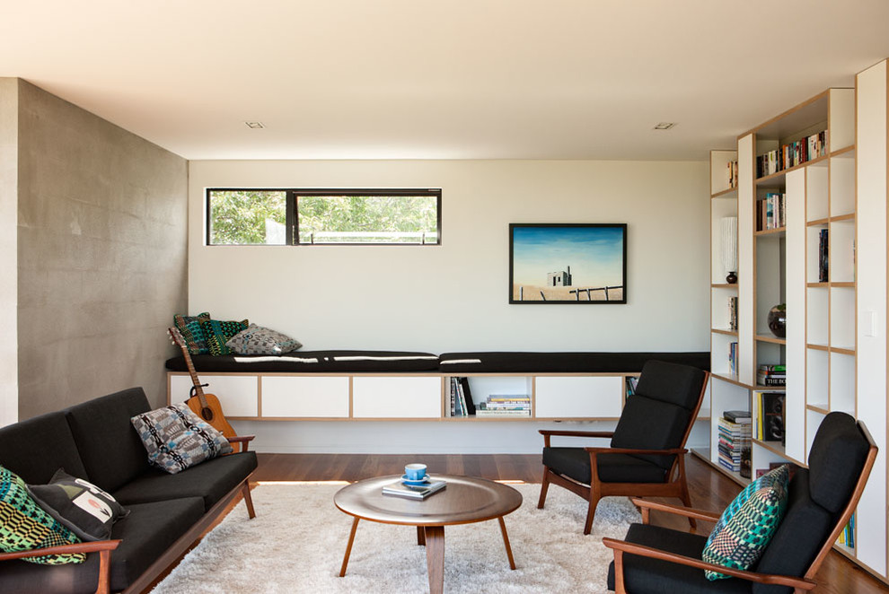 Diseño de sala de estar con biblioteca moderna con paredes blancas y suelo de madera en tonos medios