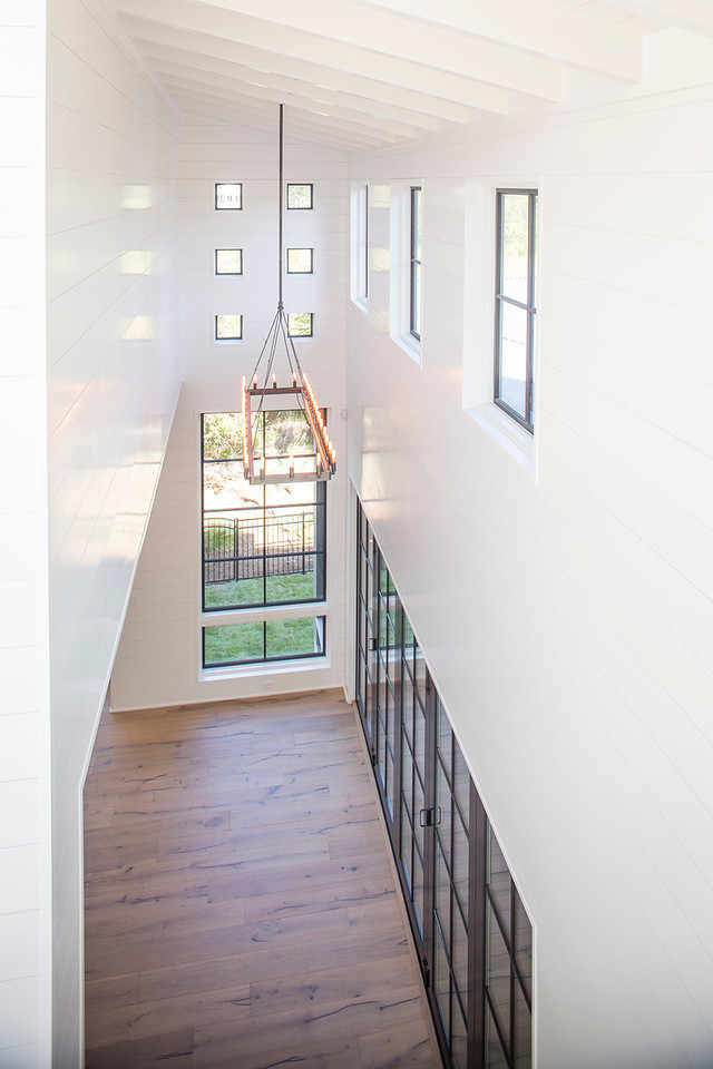 Diseño de sala de estar abierta actual grande con paredes blancas, suelo de madera clara, todas las chimeneas y televisor colgado en la pared