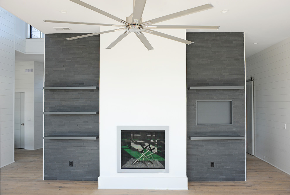 Inspiration for a large contemporary open plan games room in Charleston with white walls, light hardwood flooring, a standard fireplace and a wall mounted tv.