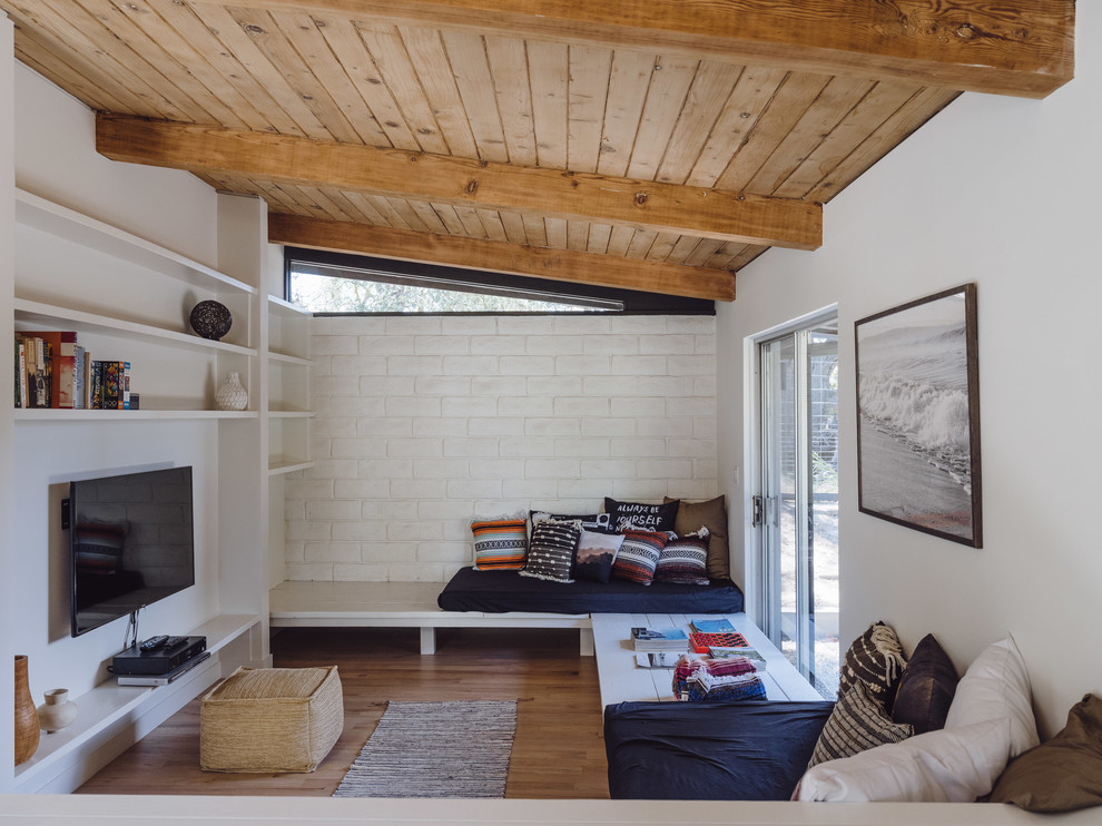 Family room - small 1960s loft-style medium tone wood floor and brown floor family room idea in Los Angeles with white walls, a wall-mounted tv and no fireplace
