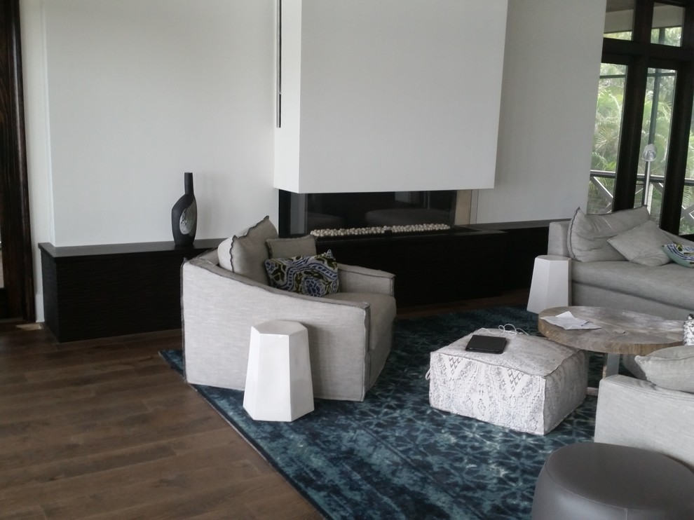 Foto de sala de estar abierta costera de tamaño medio con paredes blancas, suelo de madera clara, chimeneas suspendidas, marco de chimenea de madera y suelo beige
