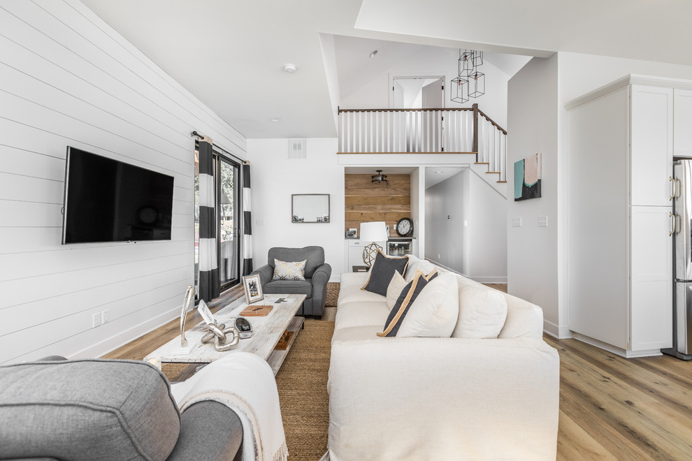 На фото: открытая гостиная комната в морском стиле с белыми стенами, светлым паркетным полом и телевизором на стене с