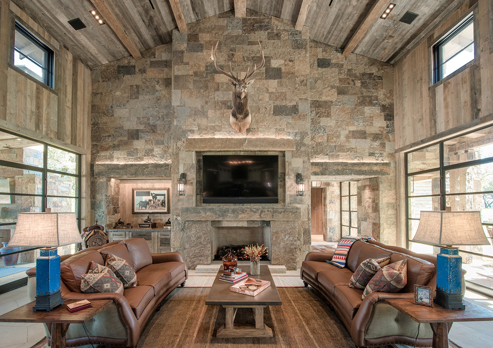 На фото: гостиная комната в стиле рустика с коричневыми стенами, стандартным камином, фасадом камина из камня и телевизором на стене с