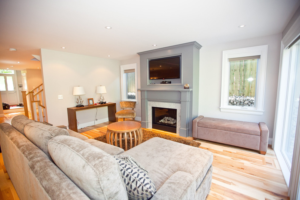 Immagine di un soggiorno tradizionale aperto con pareti grigie, parquet chiaro, camino classico e TV a parete
