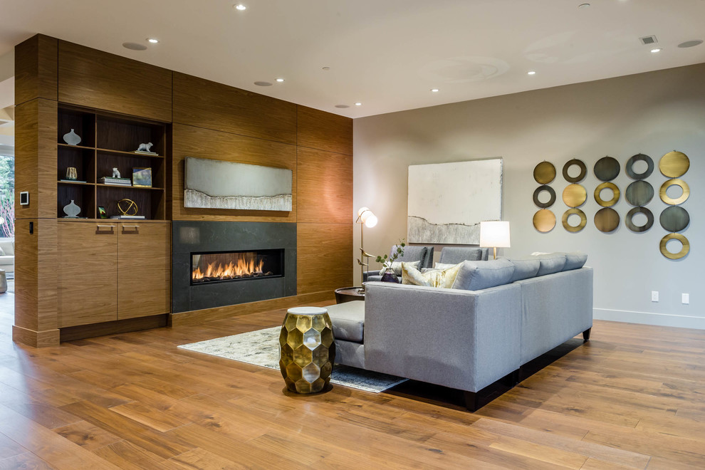 Réalisation d'une très grande salle de séjour design ouverte avec un mur beige, un sol en bois brun, une cheminée double-face et un manteau de cheminée en bois.
