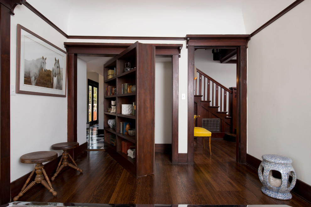 Imagen de sala de estar con biblioteca abierta de estilo americano grande sin televisor y chimenea con paredes blancas y suelo de madera oscura